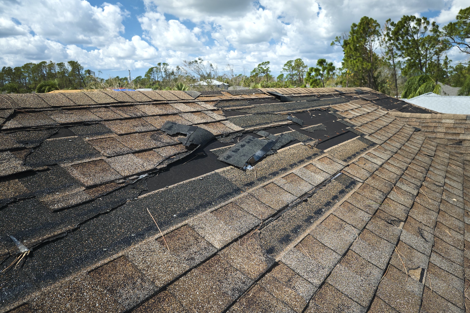 Damaged house roof with missing shingles after hurricane Ian in Florida.
